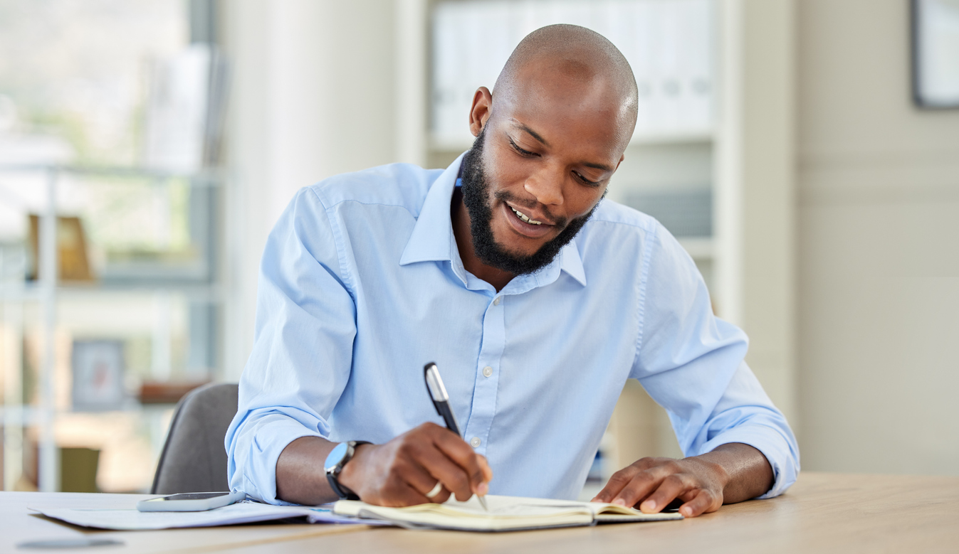 Businessman writing in a notebook while planning a strategy and working in an office. Happy male professional reading and write market search result and work updating schedule at a corporate company. Grammar Girl gives writing tips.